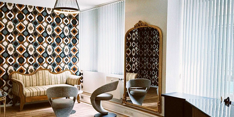 Wartebereich mit 70er-Ornamenttapete, Biedermeier-Sofa und goldenem Spiegel